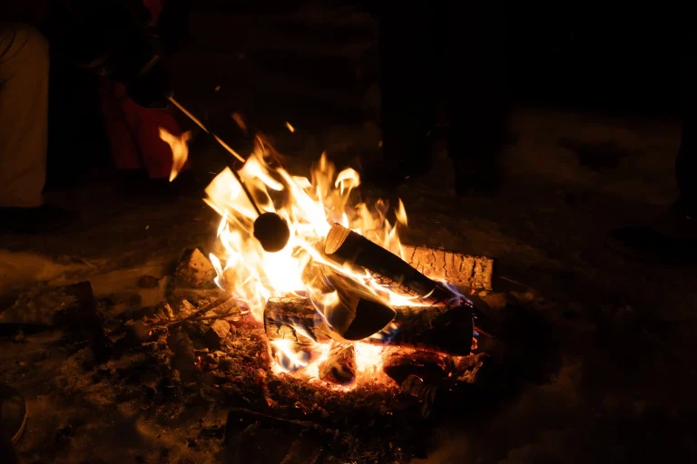 Sausage grilling over open fire on a barbecue, flames visible, outdoor cooking