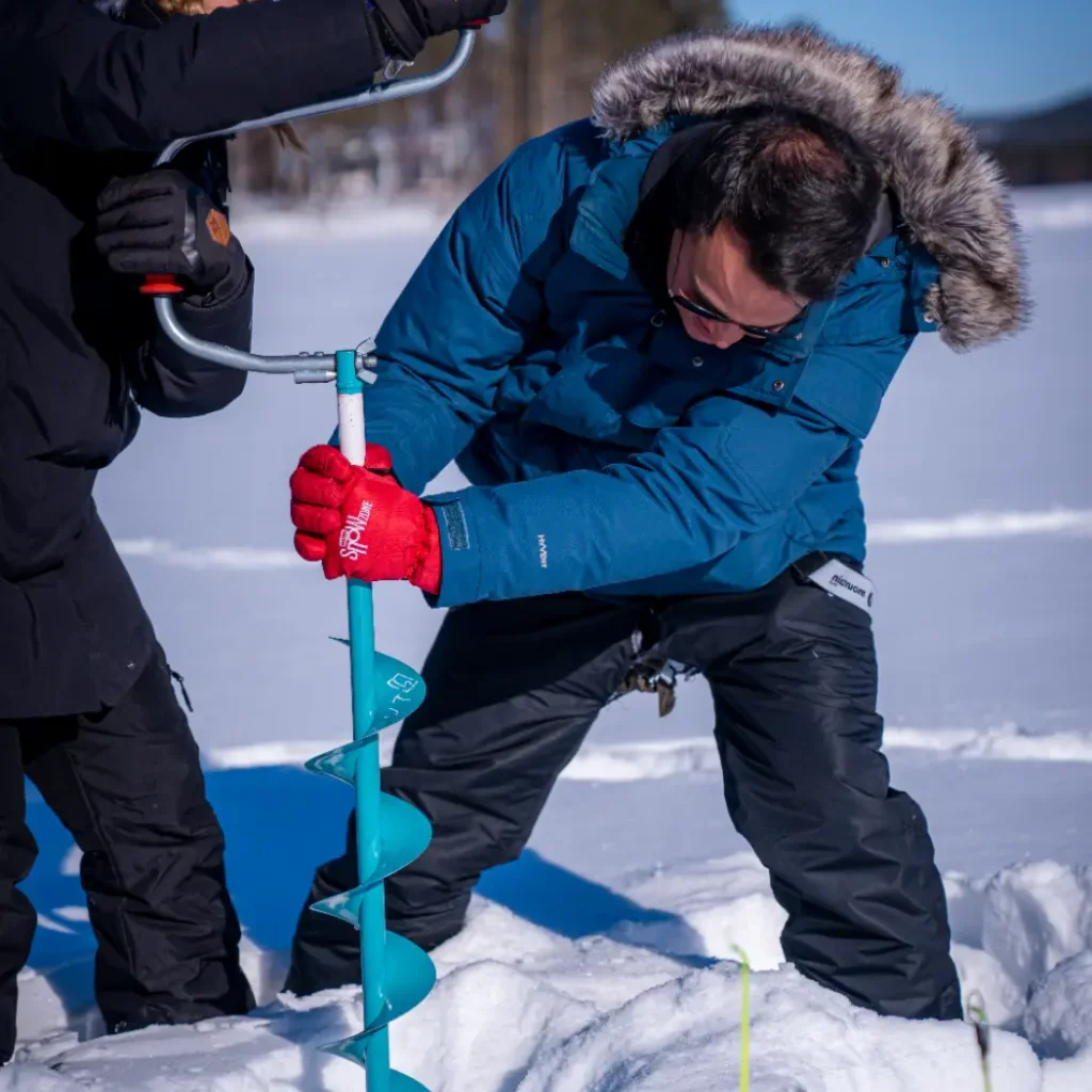 Person drilling an ice hole while ice fishing in snow-covered Lapland